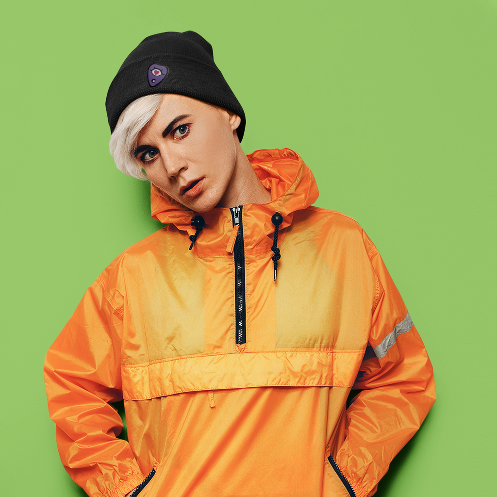 a woman with an orange wind breaker, wearing a black beanie with the planchette design from ArielAnna