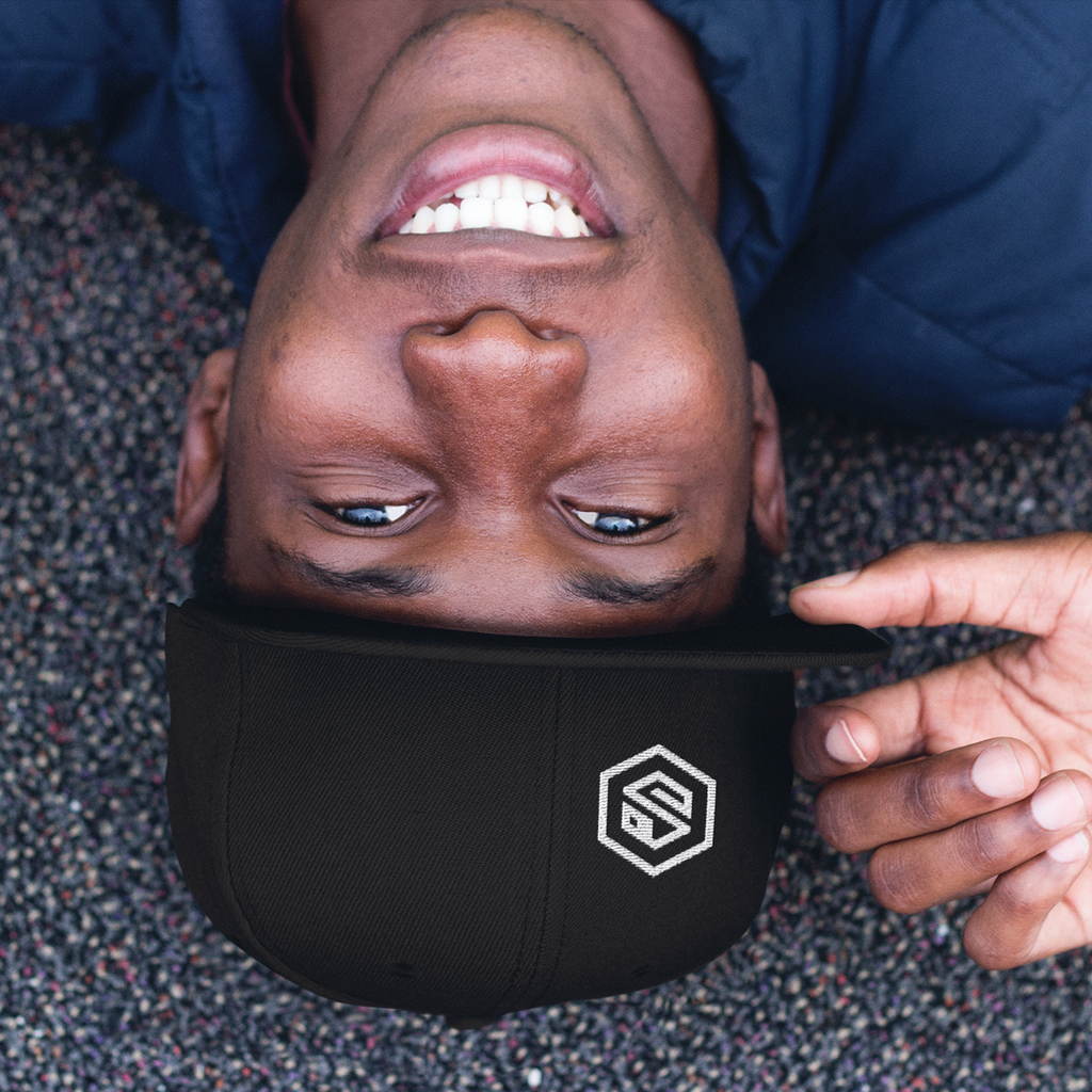 a man lying on the ground wearing a black snapback with the serpentzn logo embroidered on one side
