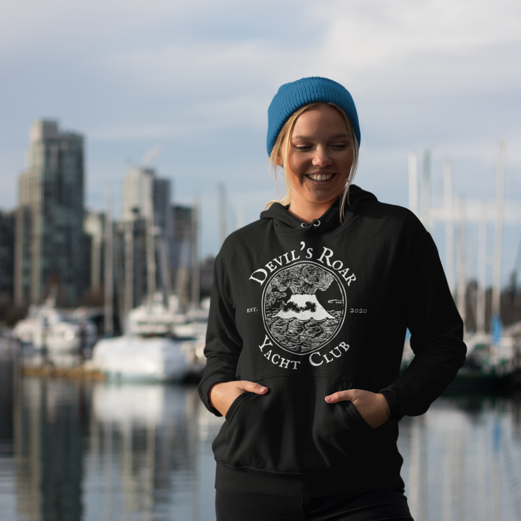 A woman standing on a pier wearing a black hoodie with the Devil's Roar Yacht Club design from Capt_Marc