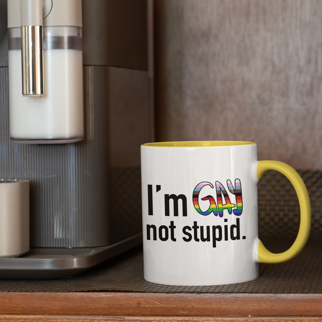 a mug next to the expresso machine, with a yellow rim and handle, the I'm Gay Not Stupid design from thezacharymike