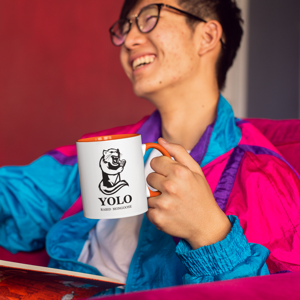 Man reading a book holding a coffee mug with orange rim and the RabidM0ngoose YOLO design on it.