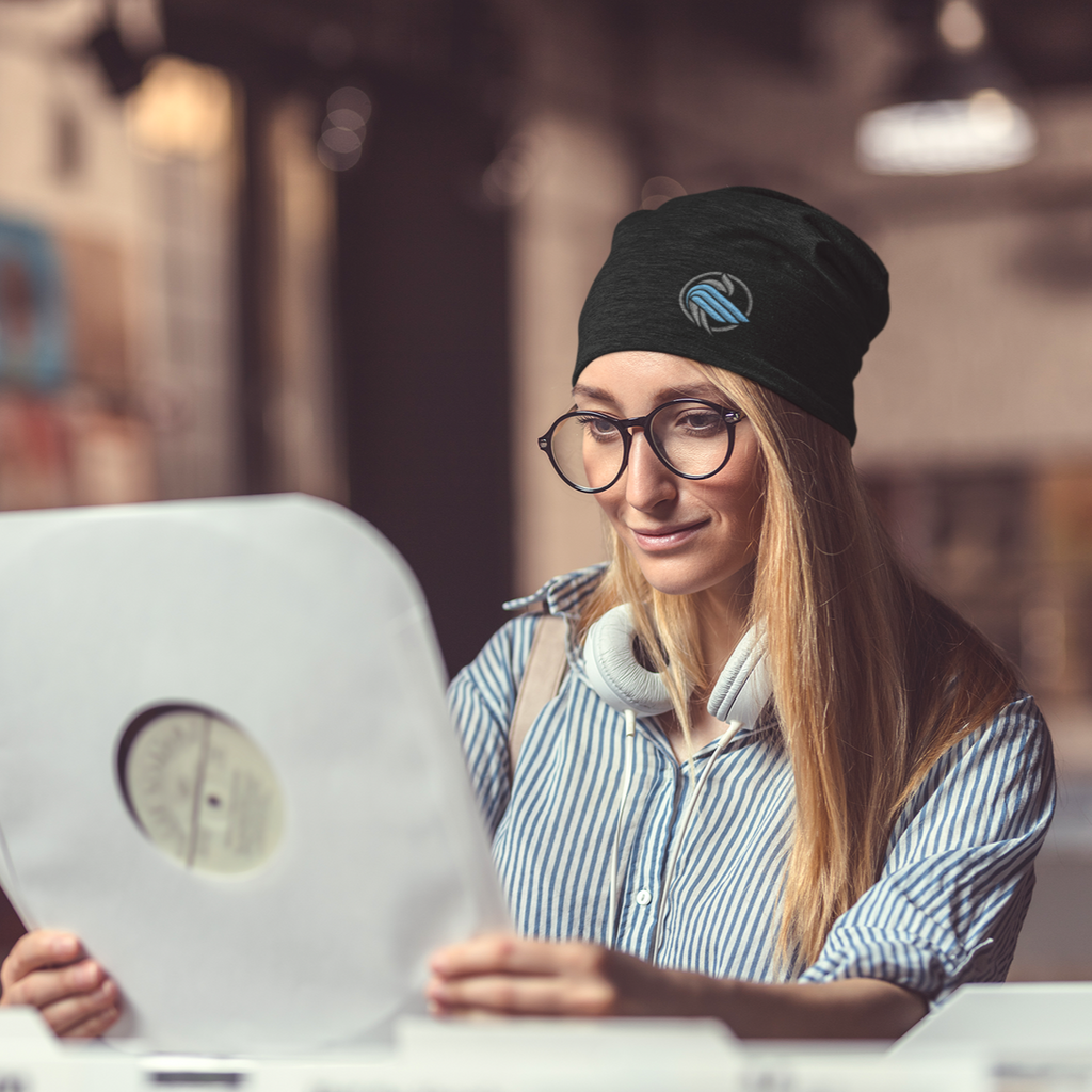 A woman looking at records in a record store wearing a black beanie with the sparrow coin embroidered on it from aBlackSparrow