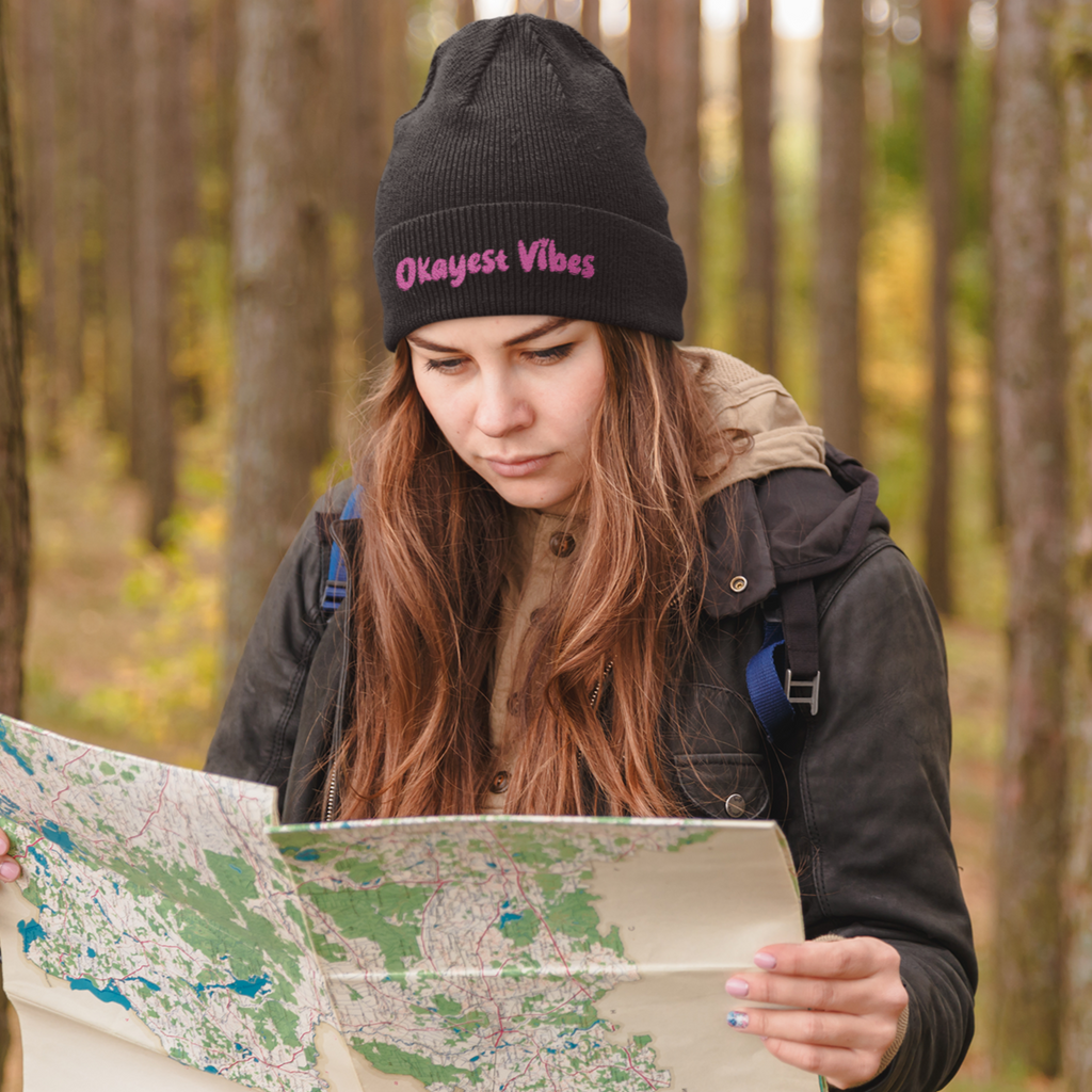 woman in the woods looking at a map, wearing a black beanie with the okayest vibes design on it.