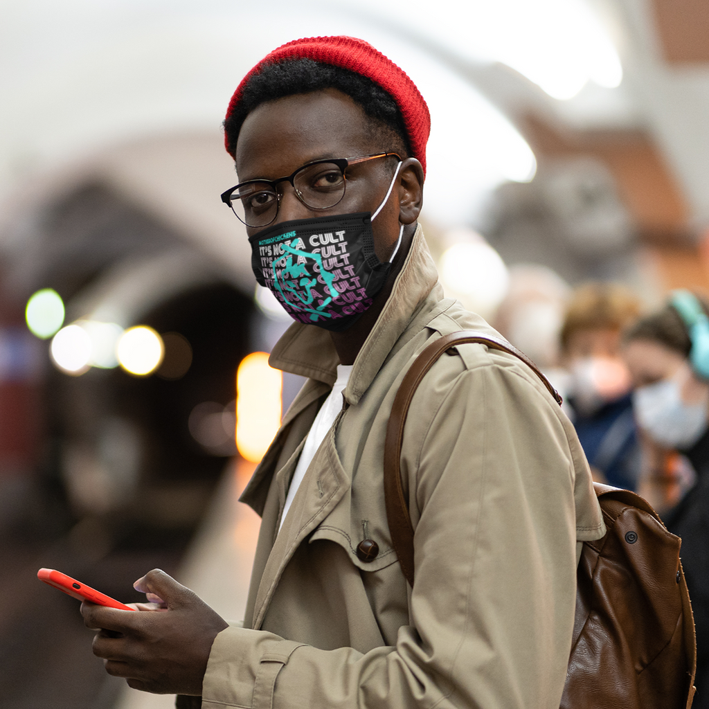 a man waiting on the train wearing a black facemask with the "It's Not A Cult" design from Mother0fChickens