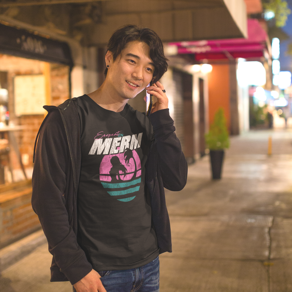 a man standing on the sidewalk and talking on a cell phone.  He is wearing a black zip up hoodie and a black tshirt with the merm design from serpentzn.