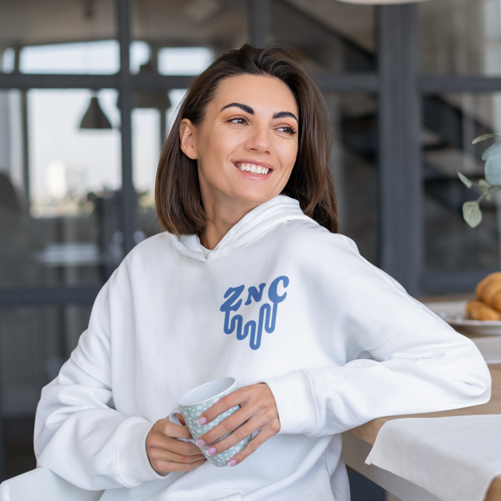a woman holding a mug, wearing a white hoodie with the melted ZNC wordmark from ZachNCheese