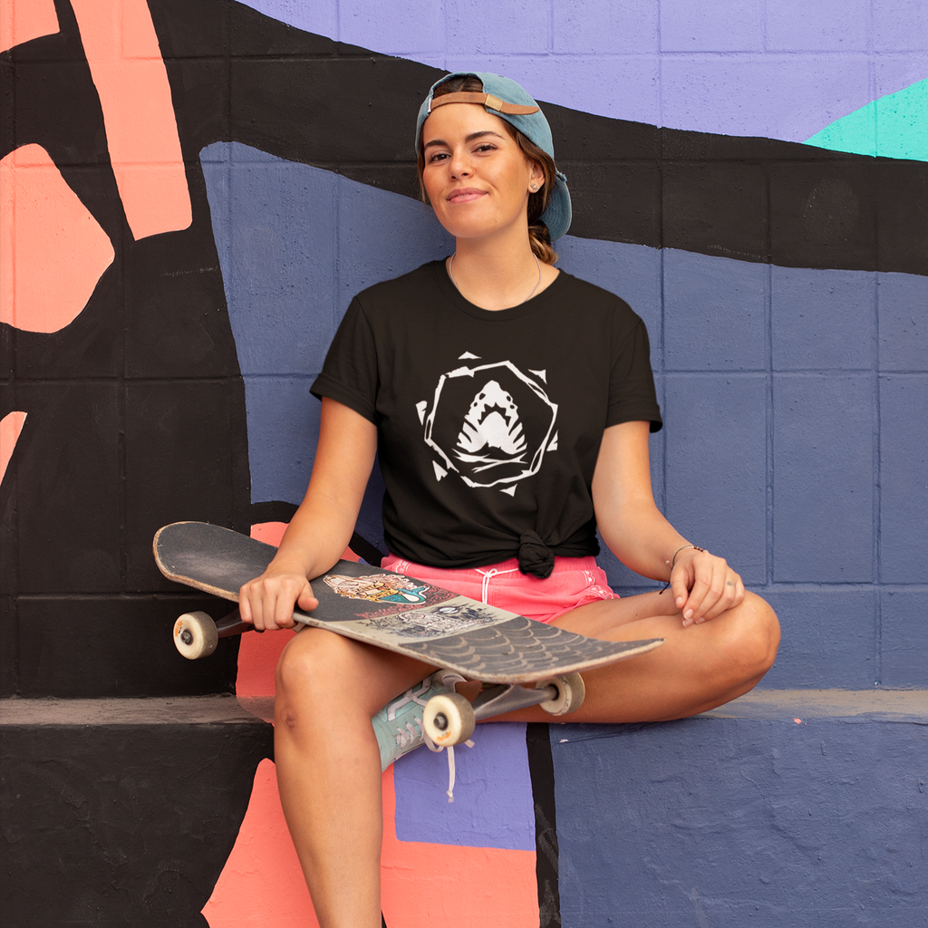 Woman with a skateboard sitting on the ledge of a skate park wearing a black foxdie megalodon tshirt