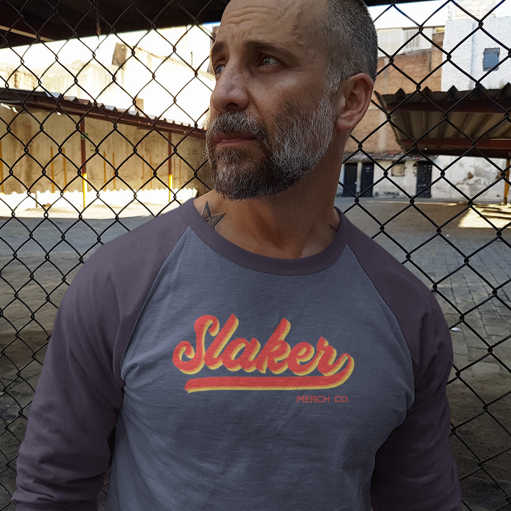 man looking away wearing a blue 3/4 sleeve tshirt with the color slaker logo on it.