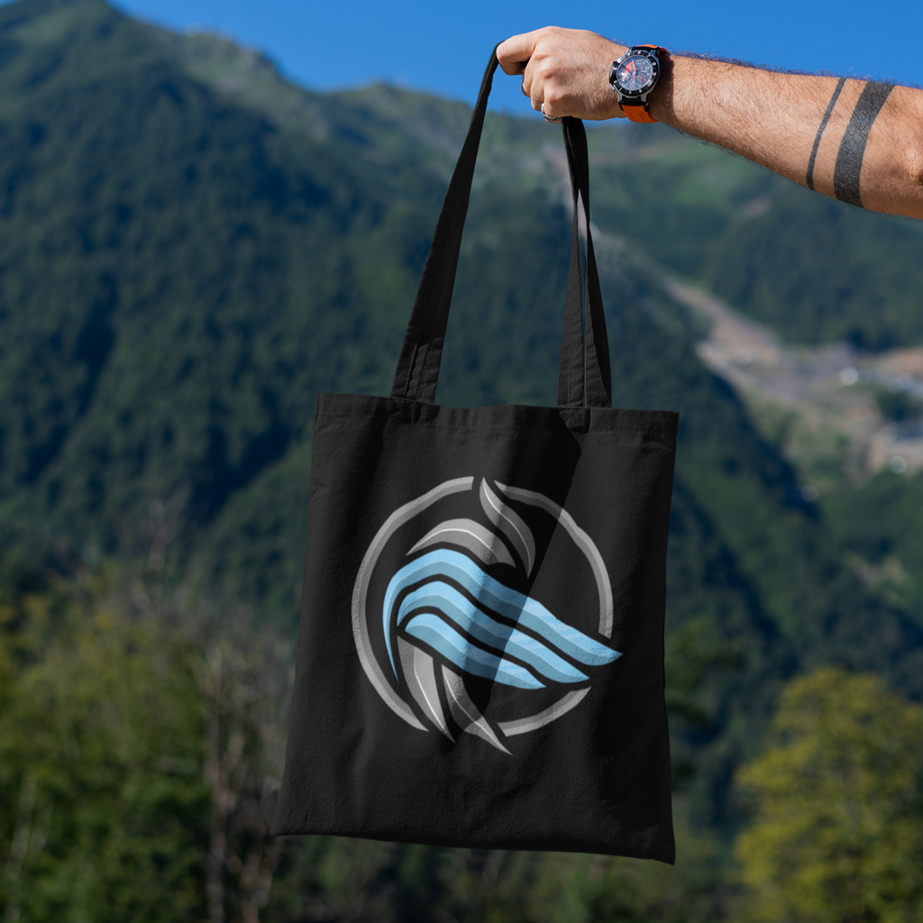 a black sparrow coin tote bag being held out in front of an outdoor scene with mountains 