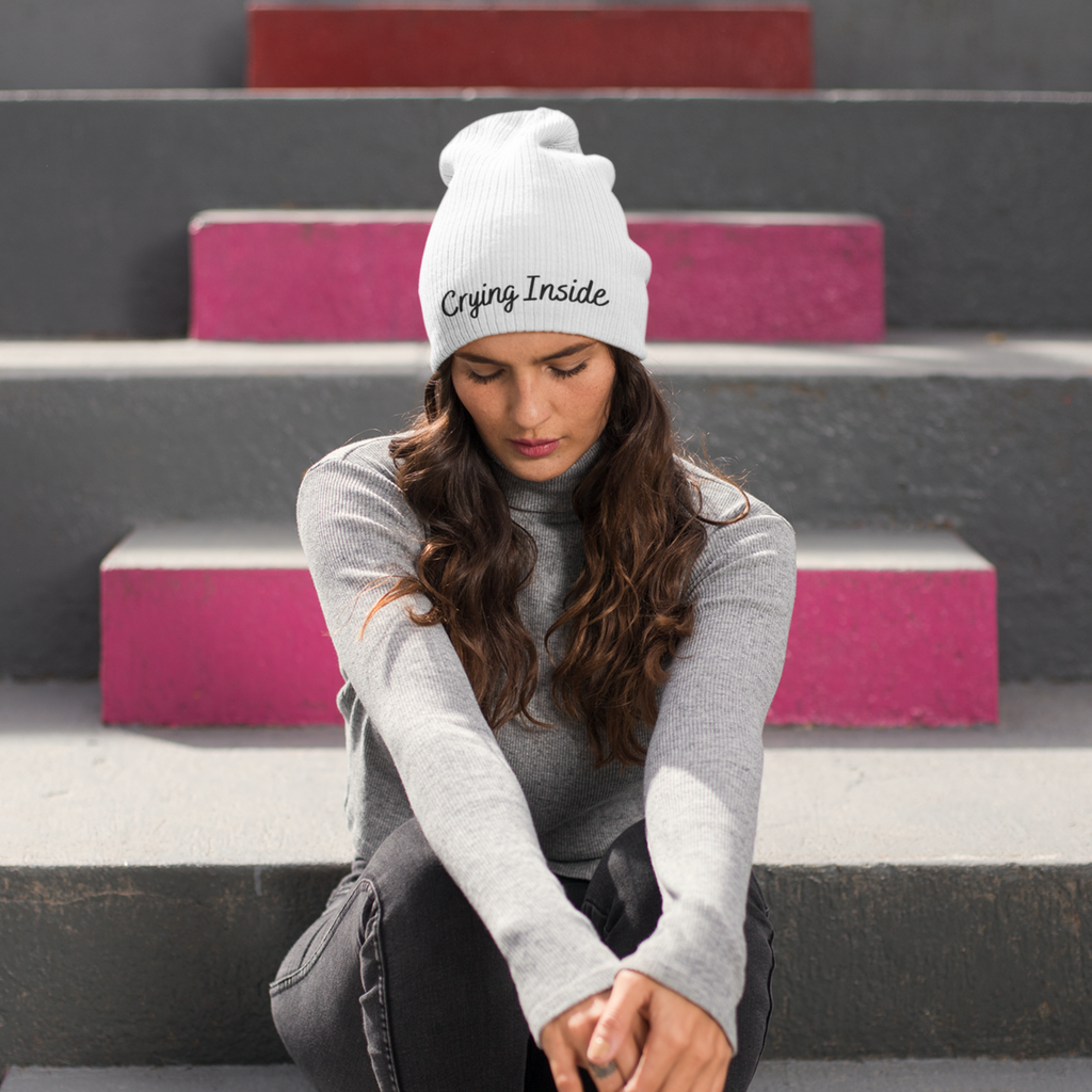 a woman sitting on stairs wearing a white beanie with the crying inside embroidery design from OhhMeggs