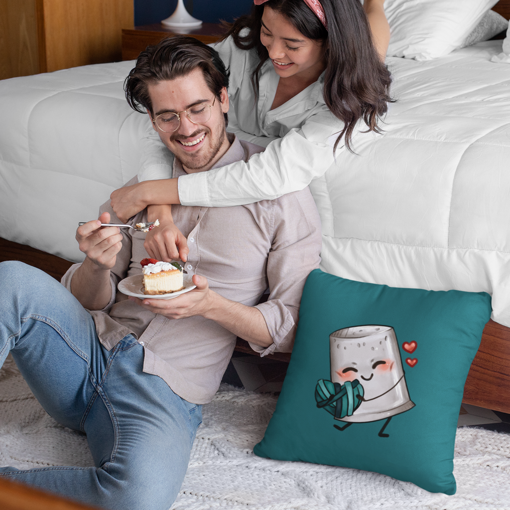 man eating cake sitting by the edge of a bed, a laying on the edge of the bed with her hands around the man.  The Brooklynne Michelle Love Fight pillow sits on the floor next to them.