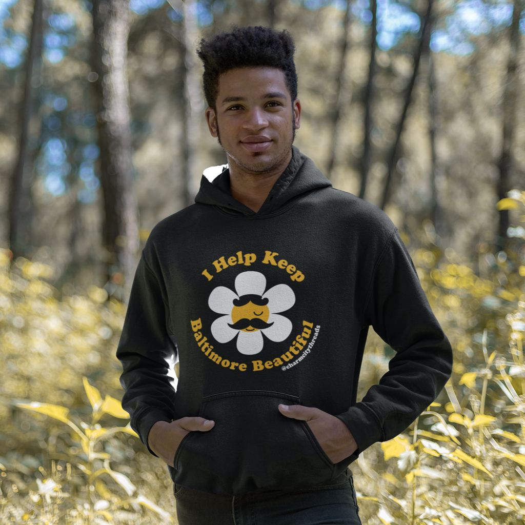 A man standing in the woods wearing a black hoodie that says "I Help Keep Baltimore Beautiful" from Charm City Threads