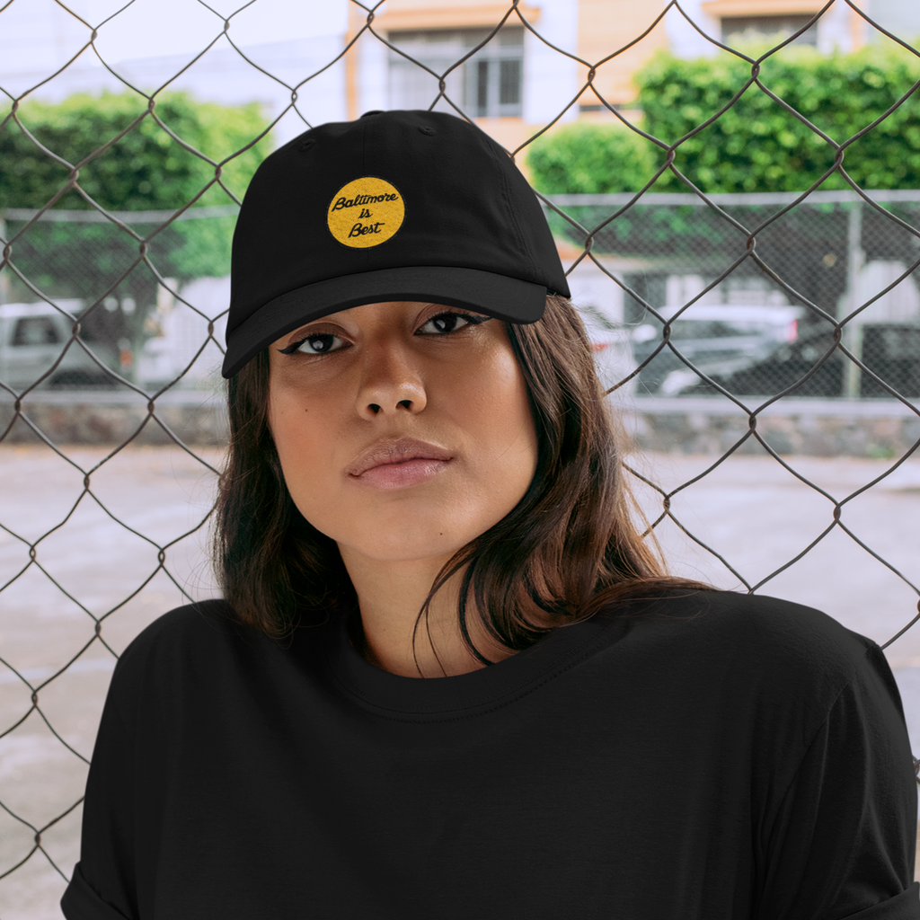 a woman wearing a black dad hat with the charm city threads Baltimore is best embroidered design