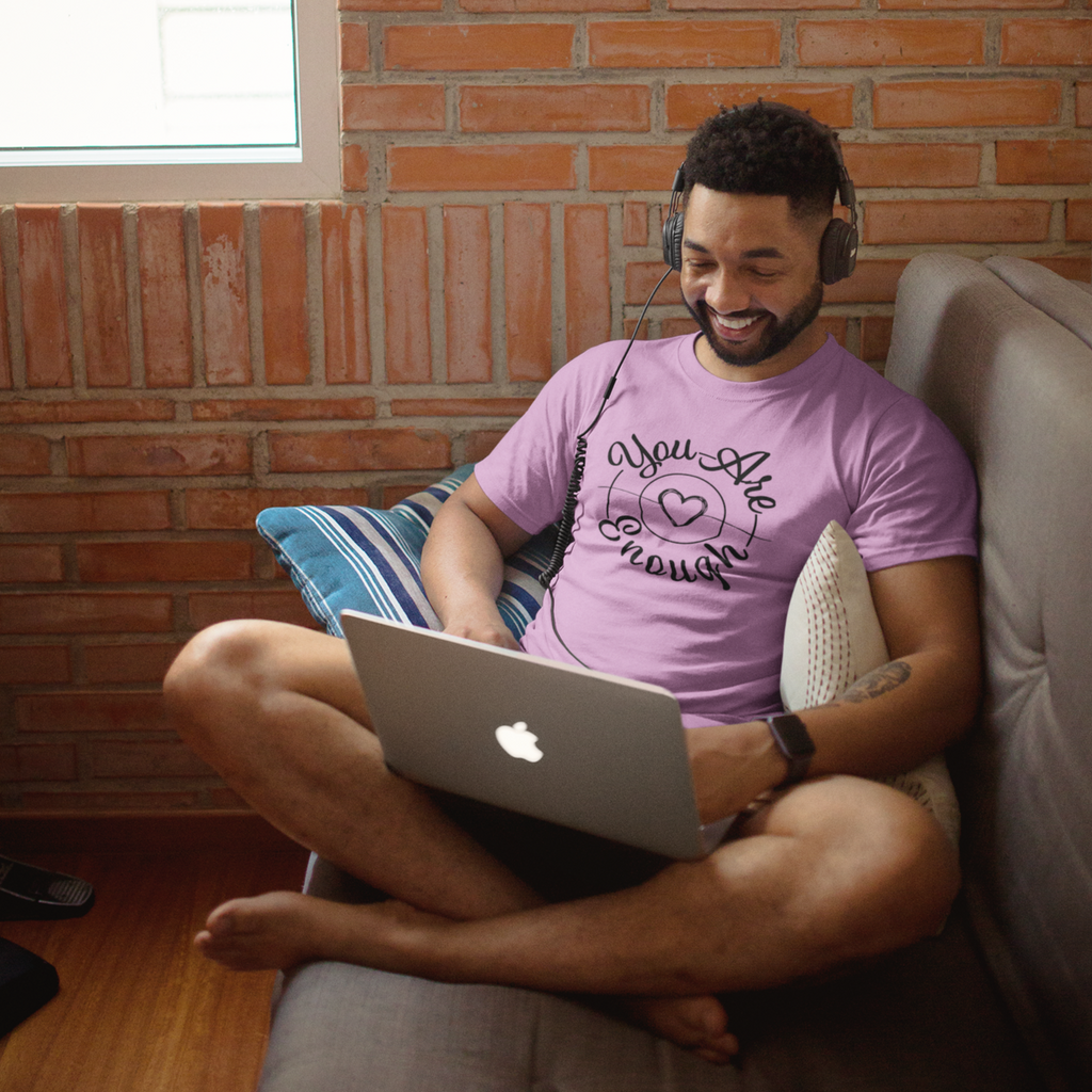 man sitting on a couch with a laptop wearing a pink shirt with the mystiraynes you are enough design.