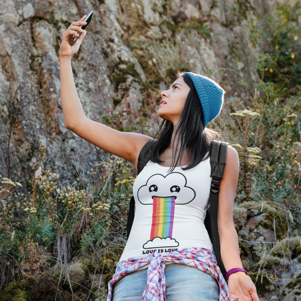 Woman hiking and looking at her cell phone.  She's wearing a white tank top with the love is love rainbow cloud.